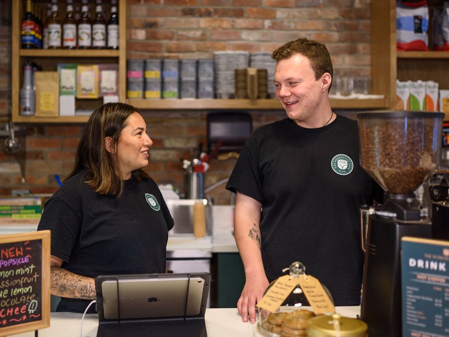 Baristas smiling and conversing behind the counter at The Rosemount Café in Toronto.