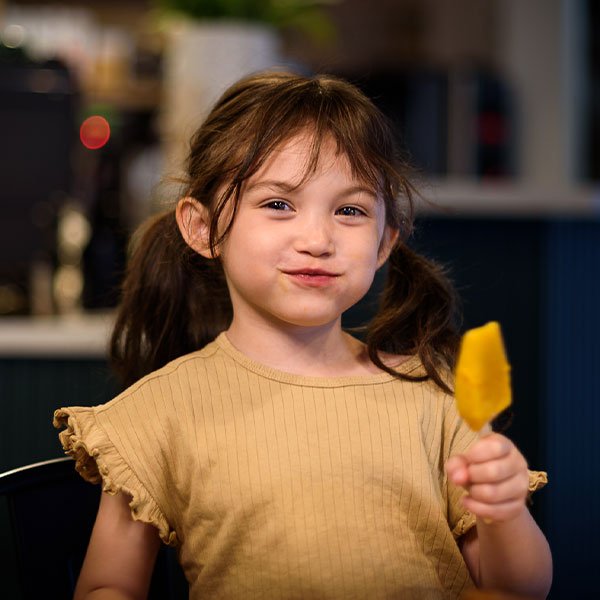 Little girl smiling and holding a popsicle at The Rosemount Cafe, a family-friendly cafe in Toronto with music and events.
